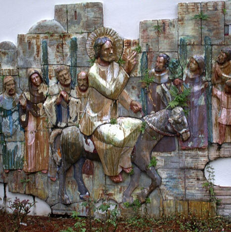 Carved relief image of Jesus riding into Jerusalem on an ass as people welcome Him. The image is life-size and colored with a water-color effect.